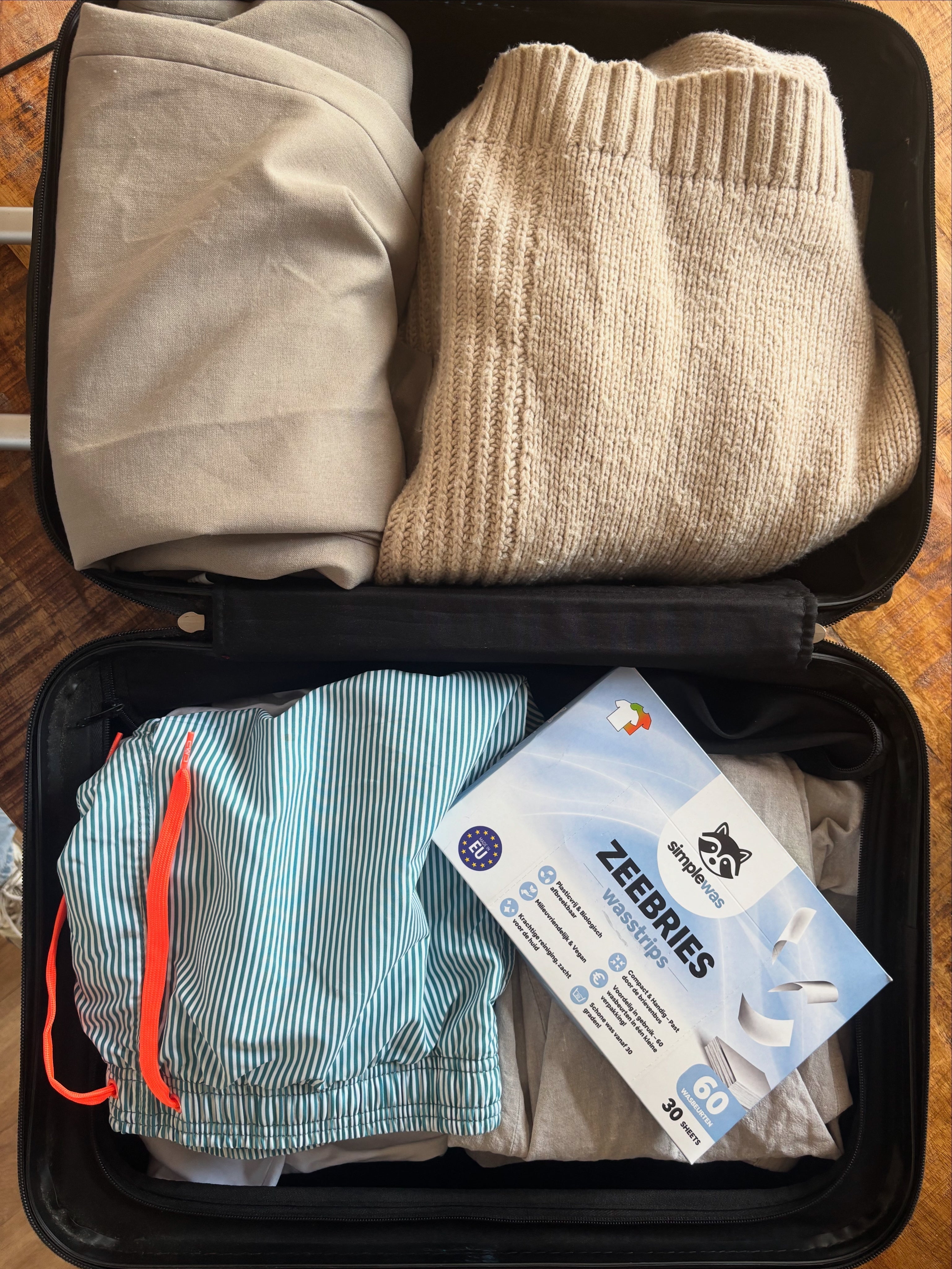 Koffer met kleding en een verpakking SimpleWas Zeebries wasstrips – compact en plasticvrij alternatief voor duurzaam wassen op reis